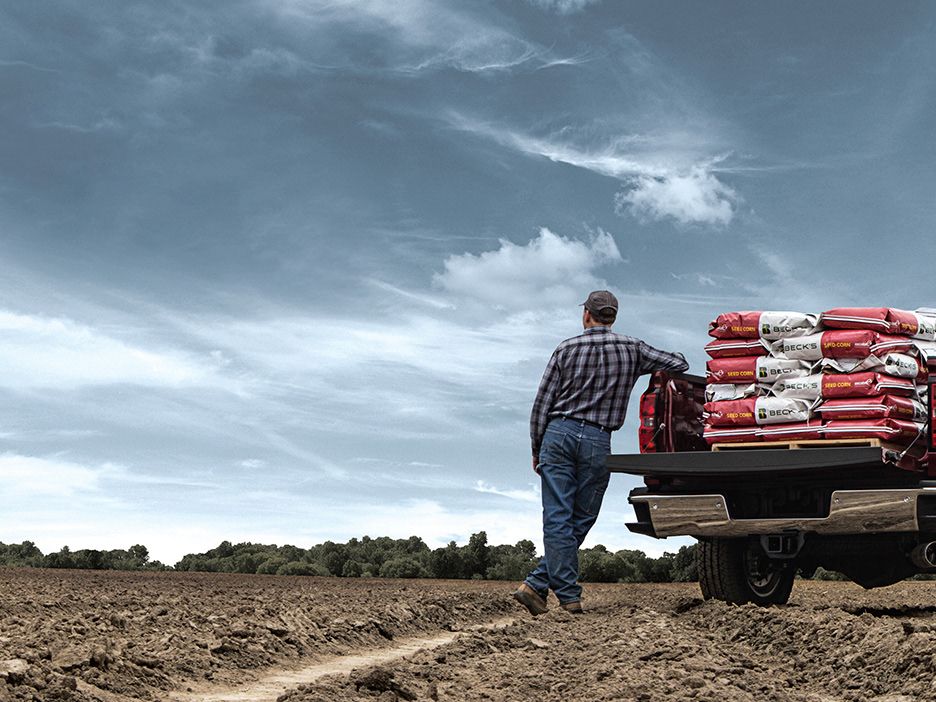 Farmer unloading seed bags from a pickup truck under a dramatic sky